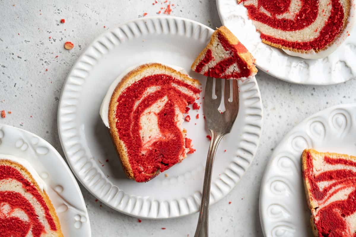 Red Velvet Marble Pound Cake slices on white dishes on the table with a fork on one plate with a piece on it.