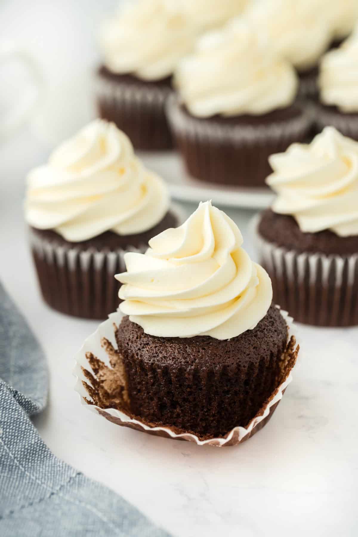 A chocolate cupcake recipe with one having the wrapper down and several in the white background