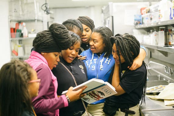 Baking students crowd together and look at Grandbaby Cakes cookbook