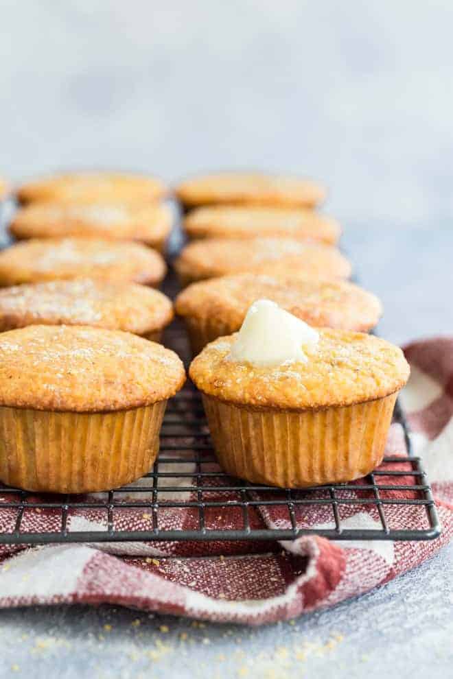 These moist, sweet and perfect corn muffin recipe is stacked on a wire rack under a red and white napkin