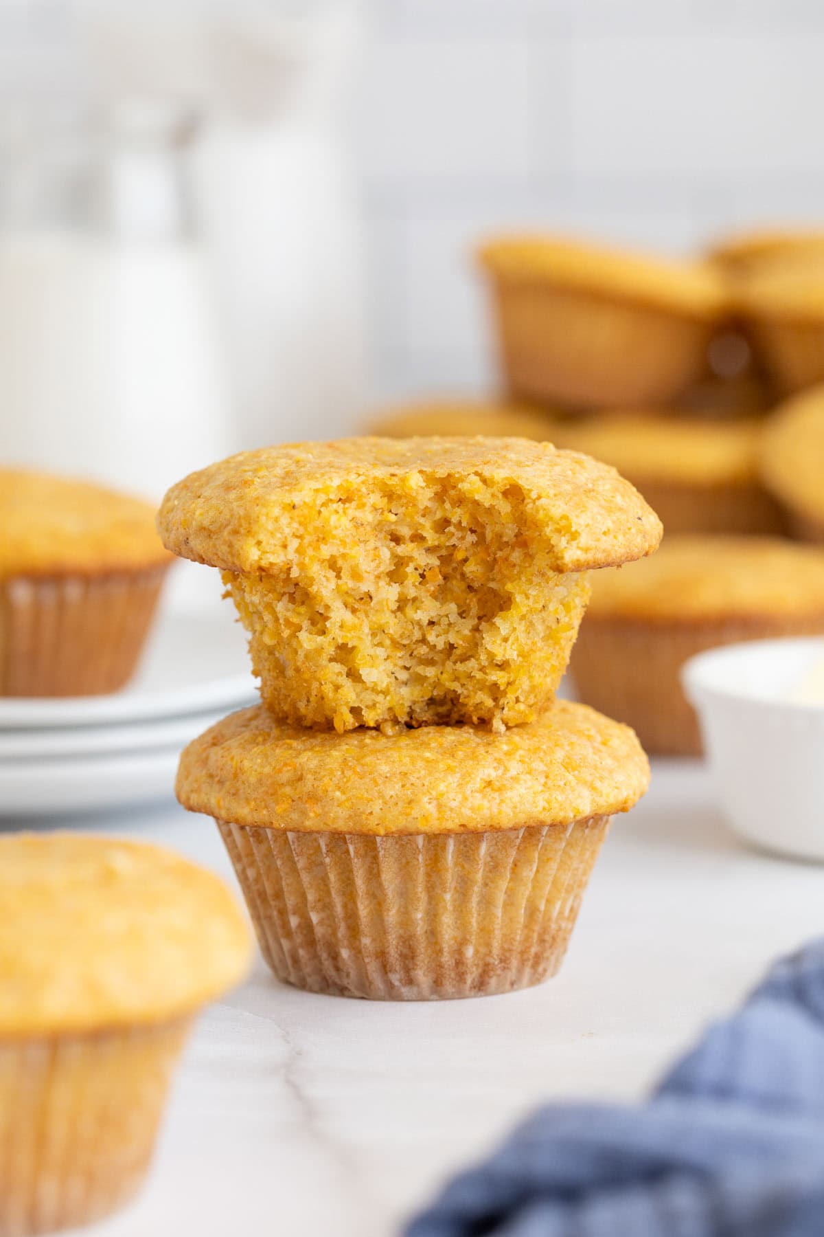 A bitten cornbread muffin stacked on another muffin with more muffins in the background