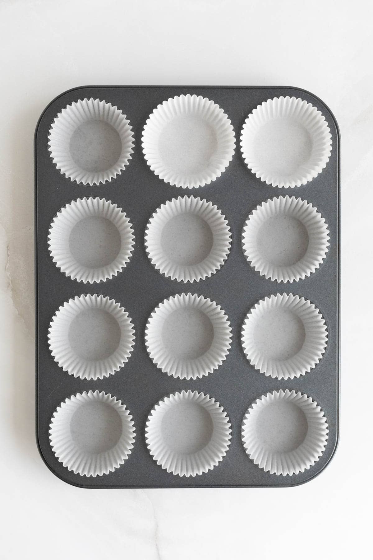 Empty muffin tin lined with white paper liners