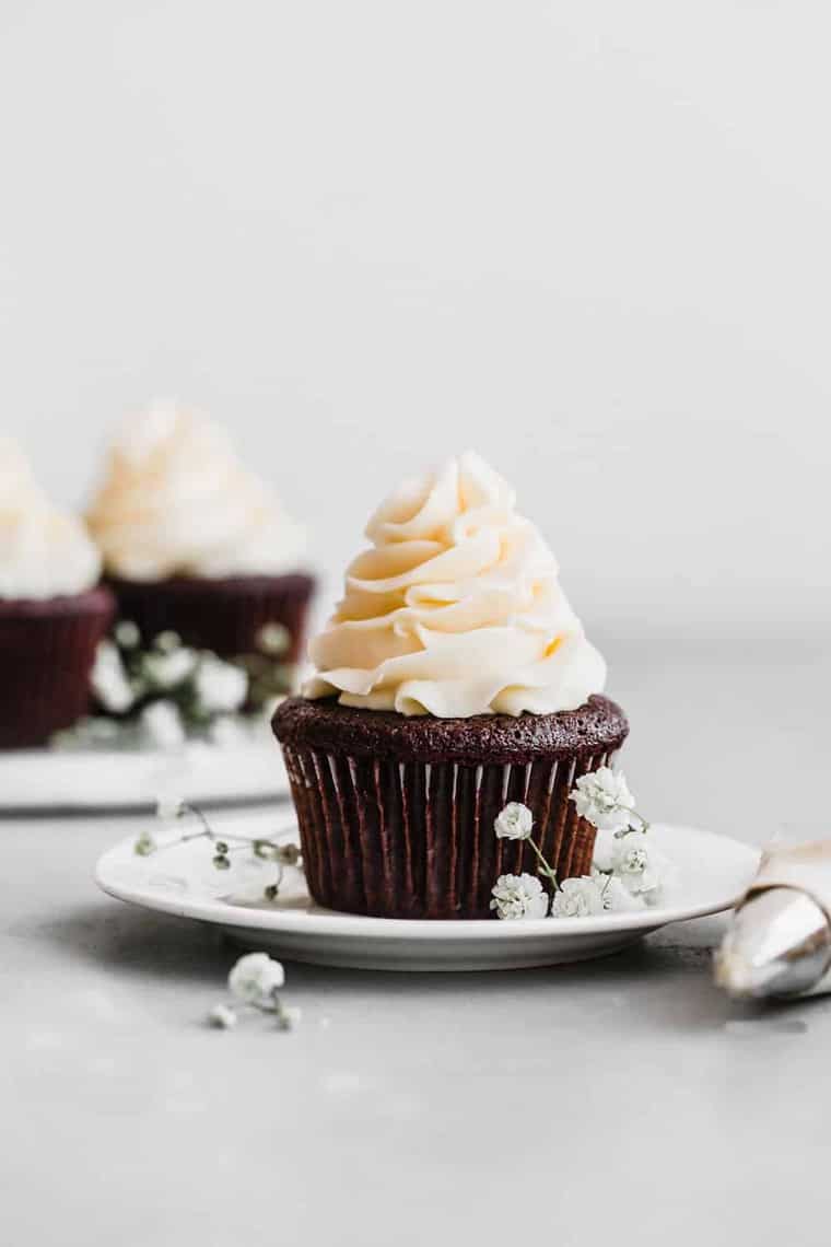 Best Chocolate Cupcake recipe with buttercream frosting on a small white plate with more in the background