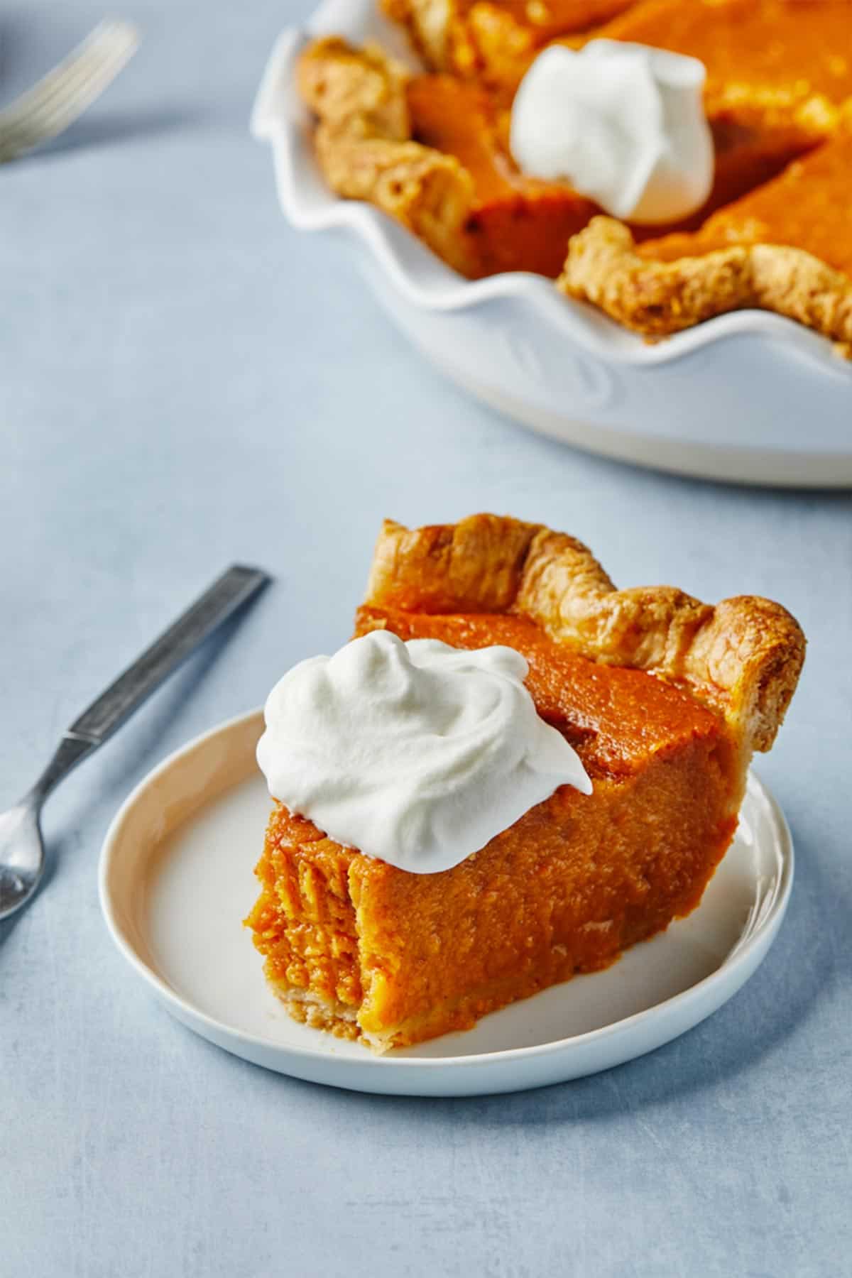 A sweet potato pie on the table with a spatula lifting a slice out.