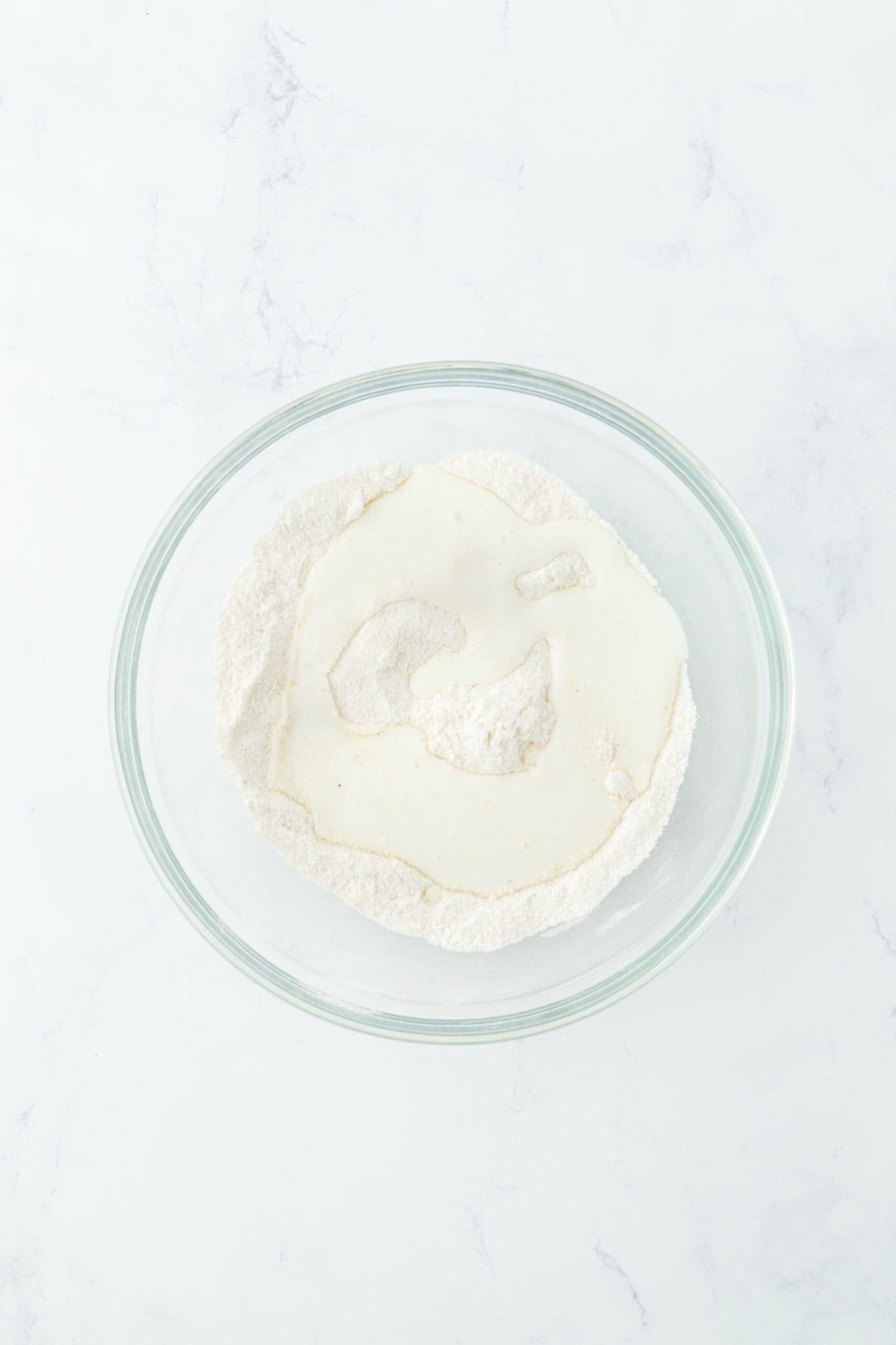 Buttermilk added to dry ingredients in a glass bowl on white countertop