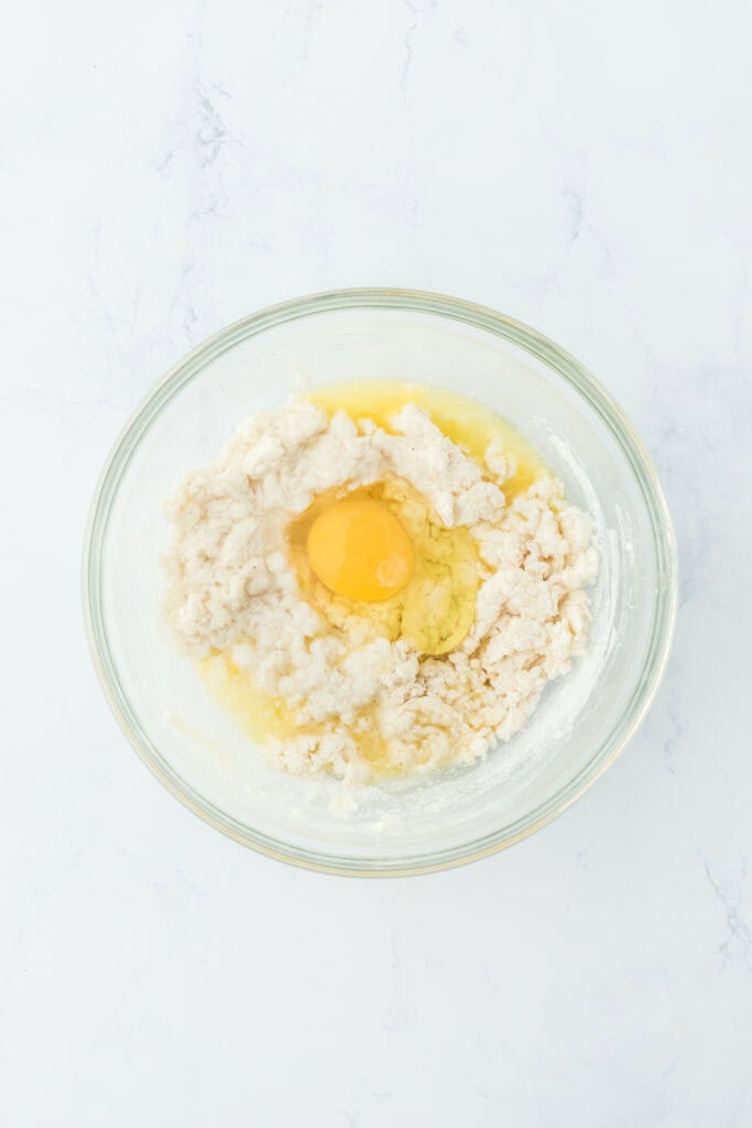 Egg added to johnny cake batter in a glass bowl on white countertop