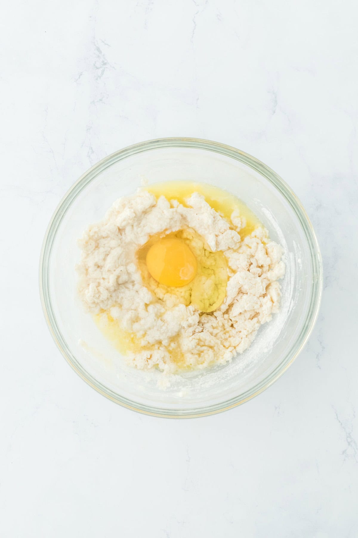 Egg added to johnny cake batter in a glass bowl on white countertop