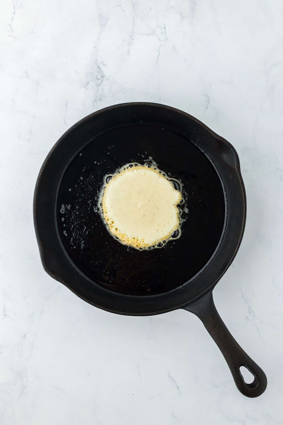 Johnny cake batter being fried in a cast iron skillet on white countertop