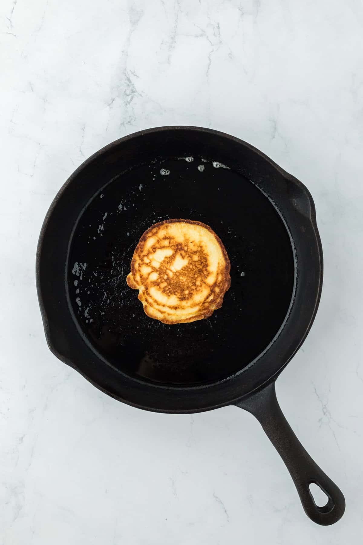 Flipped over hoe cake in a cast iron skillet being fried