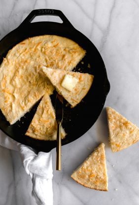 An overhead shot of a cast iron skillet with slices of Mexican cornbread with butter on top ready to serve