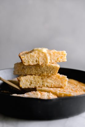 A large cast iron skillet filled with Mexican cornbread recipe slices piled high with melted butter on top #cornbread #cornbreadrecipe #mexicancornbread
