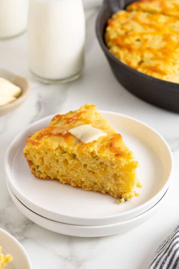 A slice of Mexican cornbread recipe on a white plate with a pat of butter