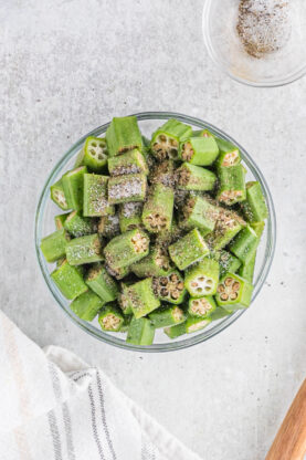 Chopped okra in a clear bowl with salt and pepper sprinkled on top