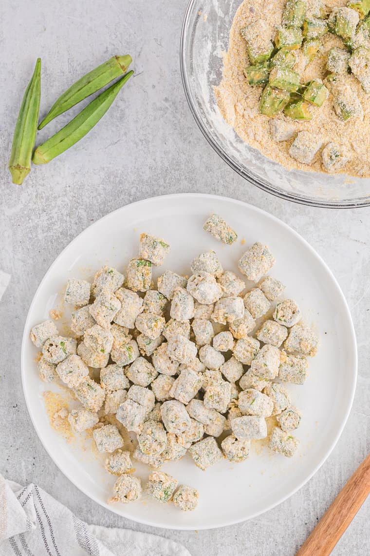 Breaded okra on a white plate before frying