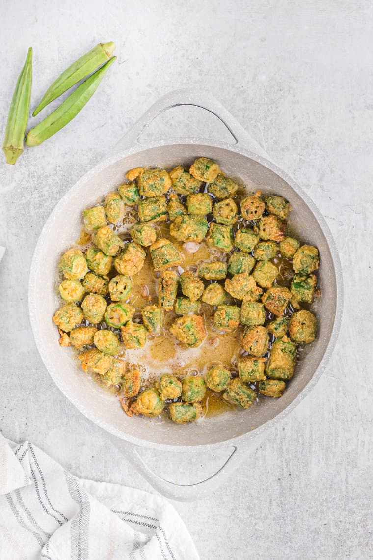 Okra frying in a white skillet