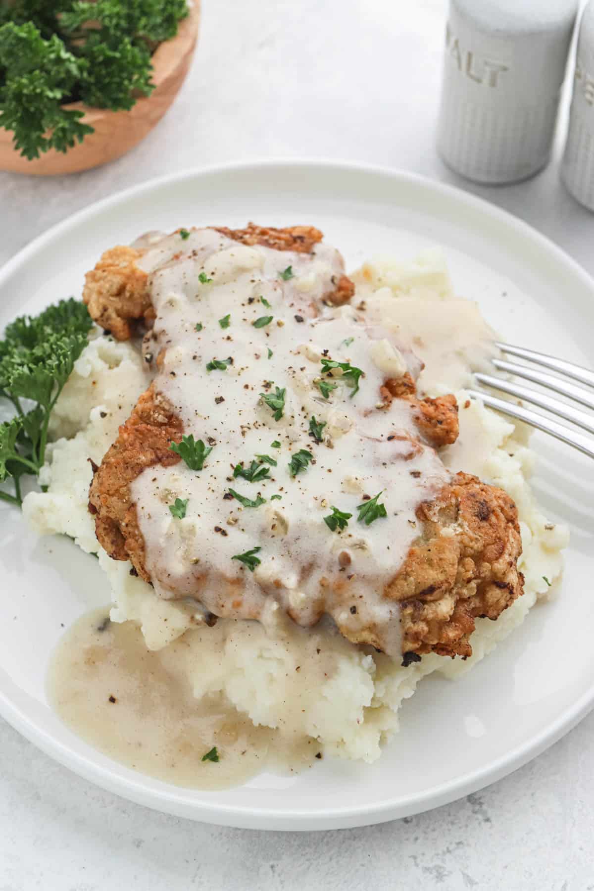 A plate of chicken fried steak on a bed of mashed potatoes covered in white gravy