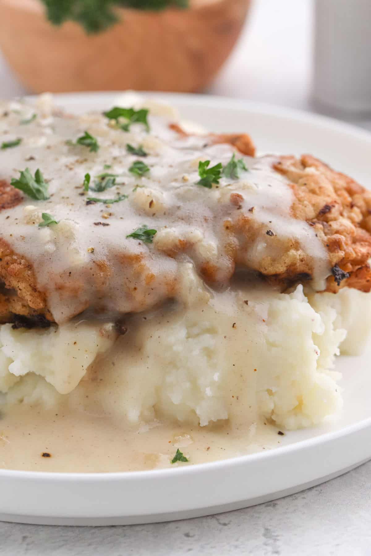 A close up of the best chicken fried steak recipe on a bed of mashed potatoes against a white background