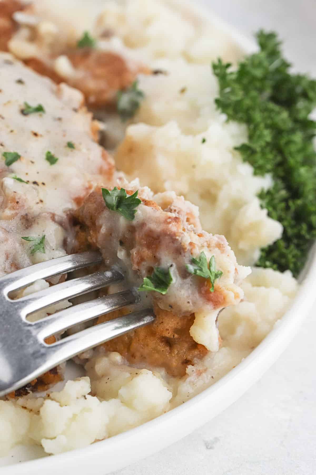 A fork lifting up a bite of chicken fried steak recipe after being cut