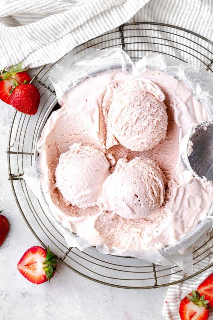 Overhead photo of three scoops of homemade strawberry ice cream against white background