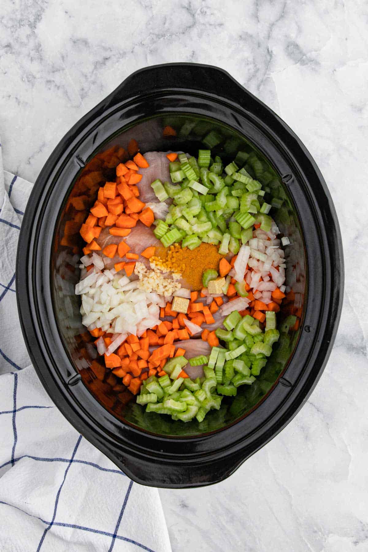 Veggies and spices added to the crockpot along with chicken breasts.
