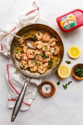 Shrimp scampi in a frying pan covered with oregano and shrimp scampi sauce.