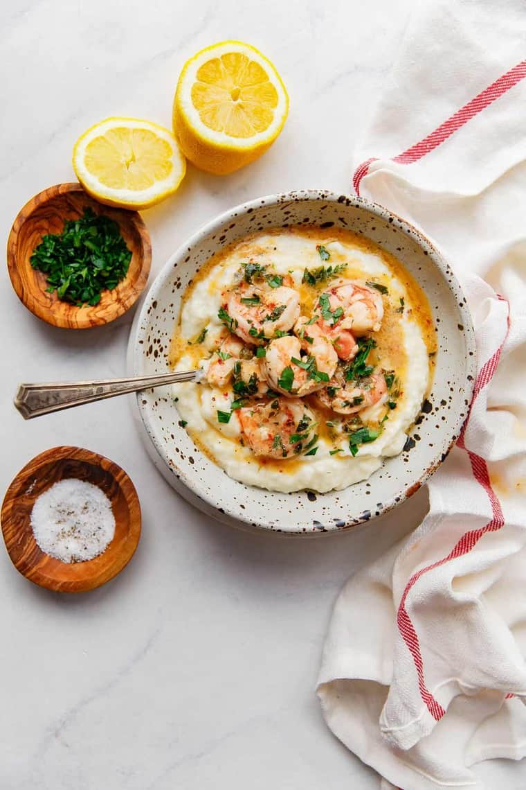 Lemon garlic shrimp scampi served over a large bowl of creamy grits with lemons surrounding