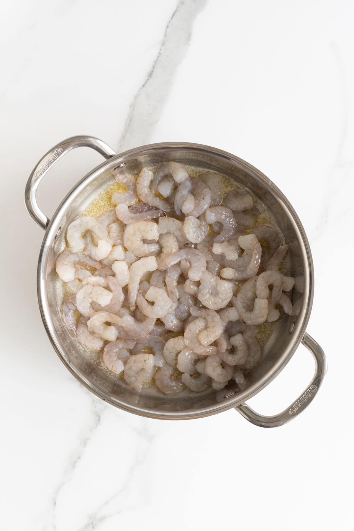Overhead shot of raw, peeled shrimp added to a stainless steel pan containing melted butter