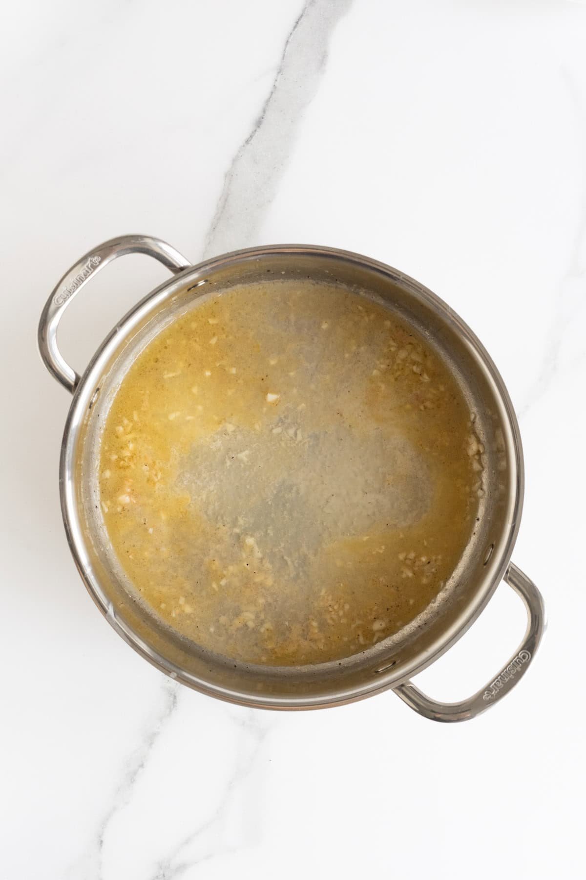 Overhead shot of a stainless steel pan containing melted butter with some small pieces of garlic visible