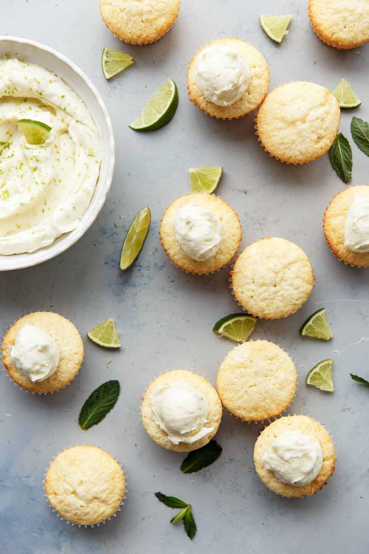 Overhead shot of several Lemon Cupcakes, some with frosting and some without next to a white bowl full of frosting