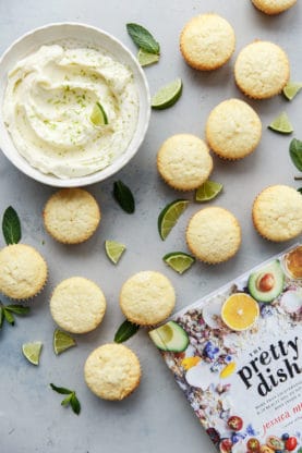 Several Lemon Cupcakes without frosting and a bowl full of frosting with the pretty dish cookbook by them