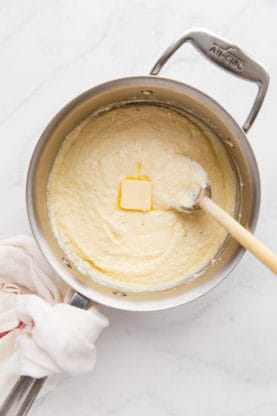 Overhead shot of a large pot of creamy Southern grits with butter melting in it along with a large wooden spoon