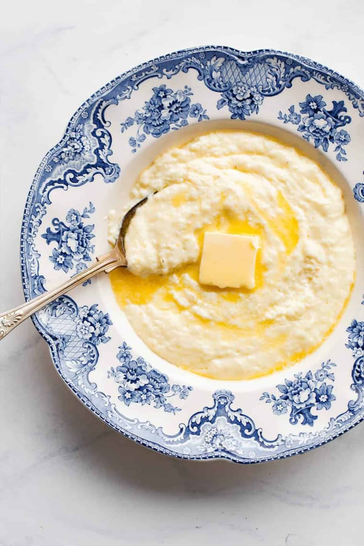 Close up of hot grits with melting butter on top served in a blue and white bowl with a spoon