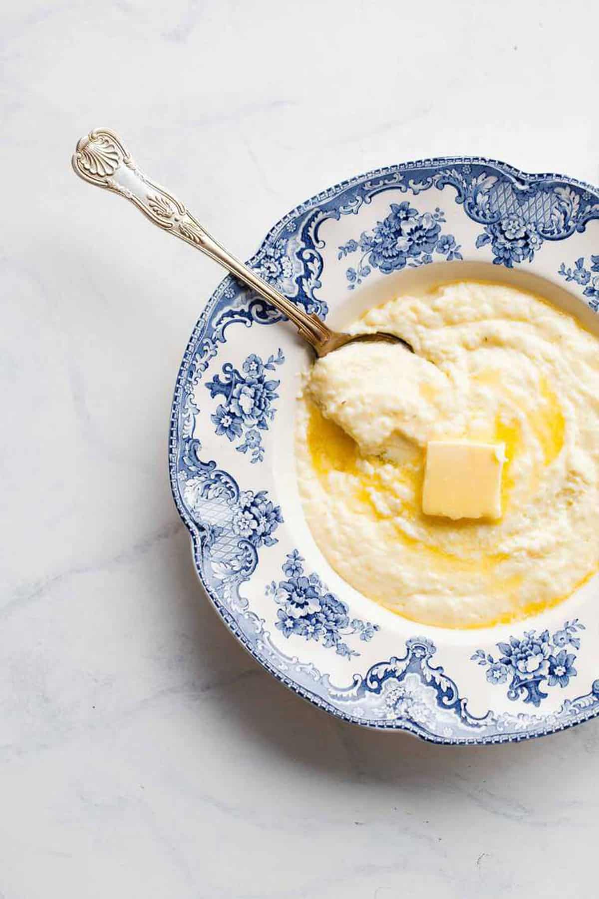 Overhead shot of hot grits with melting butter on top served in a blue and white bowl with a spoon.