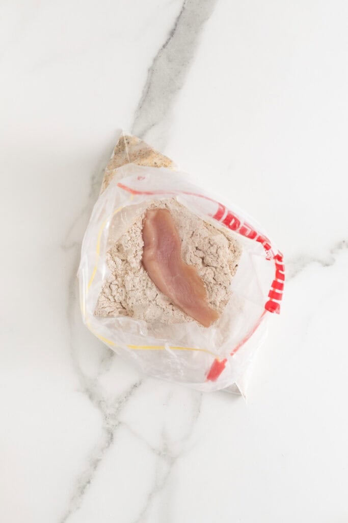 Chicken added to seasoned flour to dredge