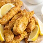 Crispy oven fried chicken on a white platter with lemon wedges ready to serve