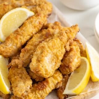 Crispy oven fried chicken on a white platter with lemon wedges ready to serve