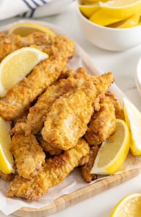Crispy oven fried chicken on a white platter with lemon wedges ready to serve