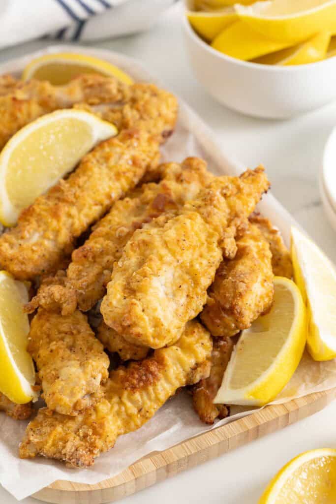 Crispy oven fried chicken on a white platter with lemon wedges ready to serve