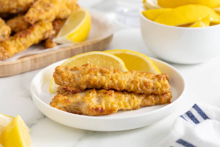 Oven fried chicken on a white plate with lemon wedges