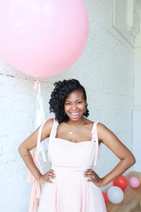 Jocelyn smiling while standing and with her hands on her hips with a pink balloon in the background celebrating her first Mother's Day