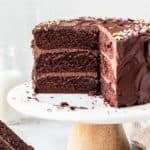 A sliced into chocolate birthday cake on white cake stand