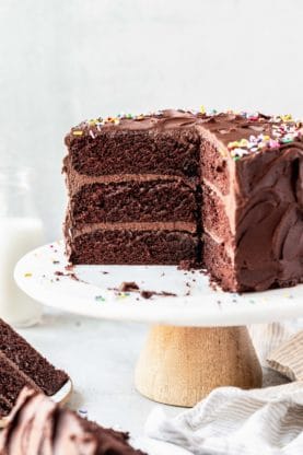 A sliced into chocolate birthday cake on white cake stand