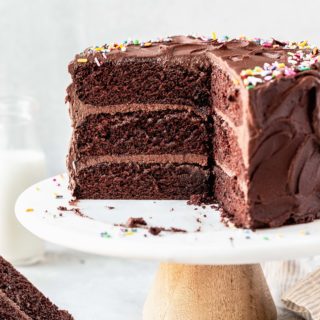 A sliced into chocolate birthday cake on white cake stand