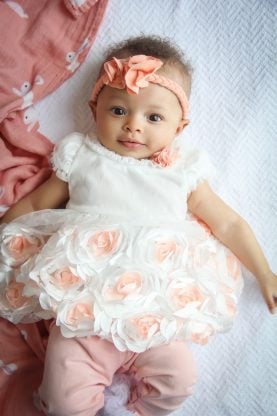 Three Months Old Baby Cakes Harmony smiling and dressed in a white and peach dress and pink pants