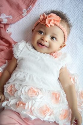 Close up of Three Months Old Baby Cakes Harmony smiling and dressed in a white and peach dress and a peach flower headband around her forehead
