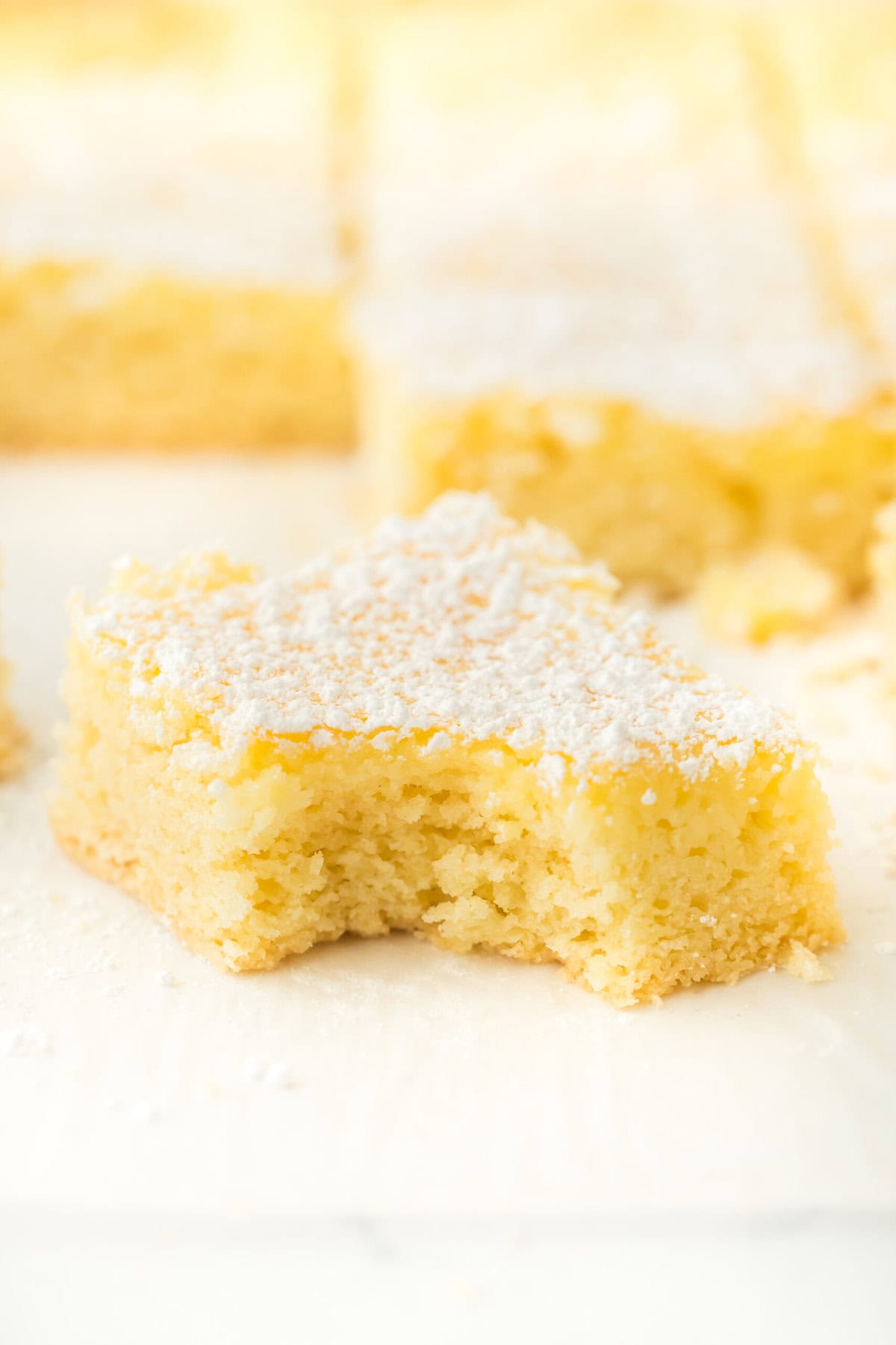 Original gooey butter cake slice with a bite on it with slices in white background with powdered sugar on top