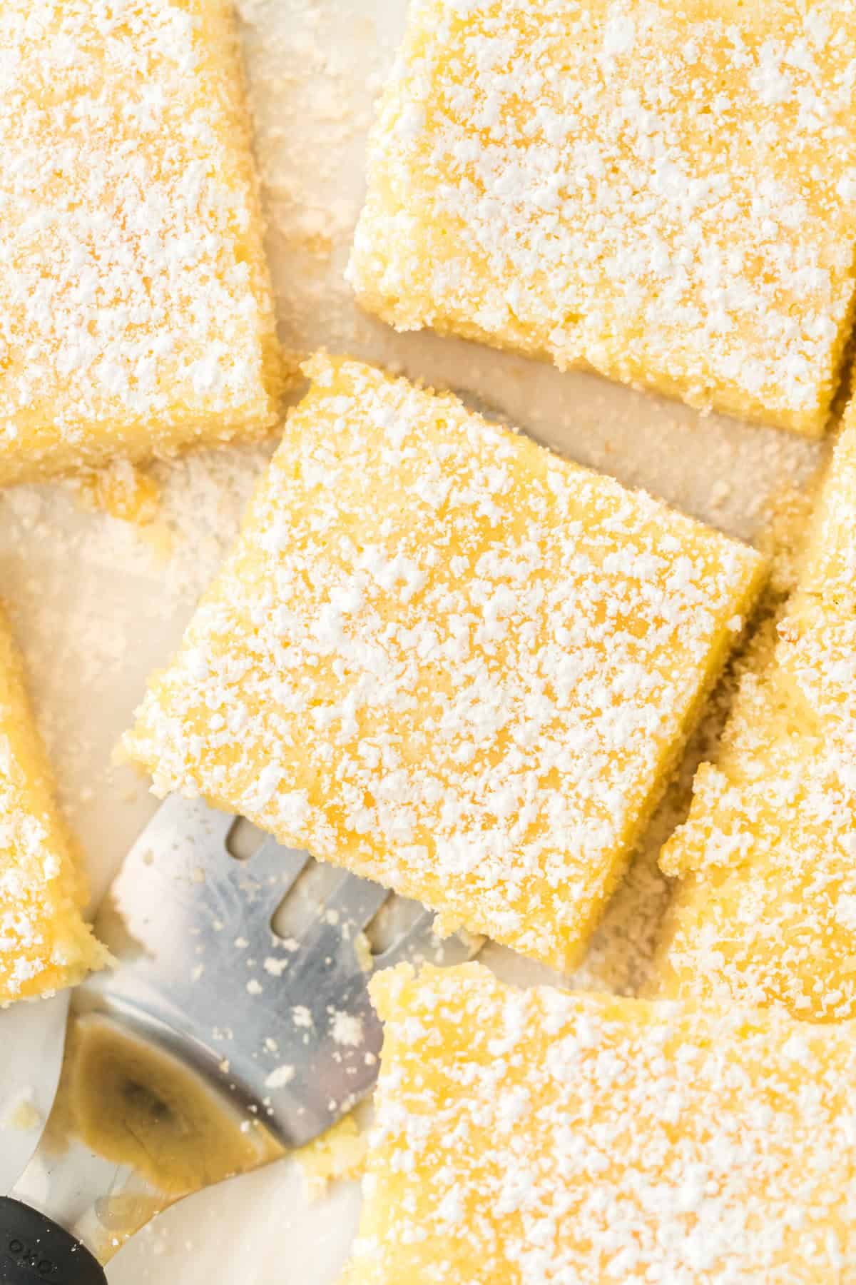 Slices of ooey gooey butter cake with powdered sugar overhead with a spatula serving one