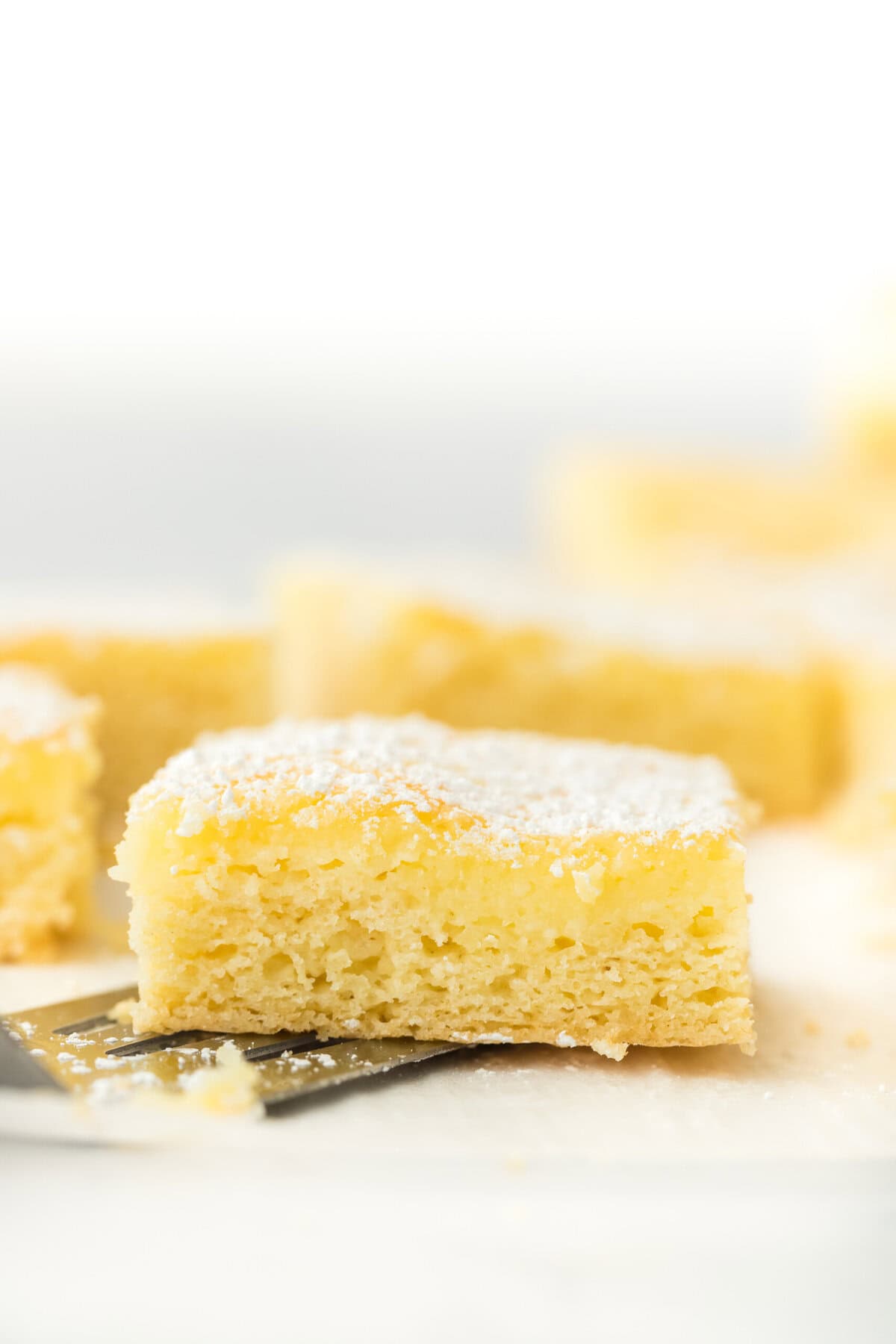 A spatula under a slice of gooey butter cake recipe with some slices in the white background
