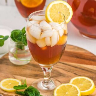 Two glasses filled with ice and sweet tea with lemon wedges on the side sitting on a wooden cutting board with mint nearby