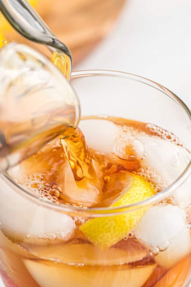 A close up of sweetened tea being poured into a large pitcher